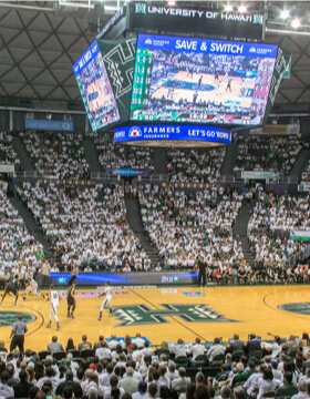 college basketball game in a full arena showing Farmers Insurance on overhead.